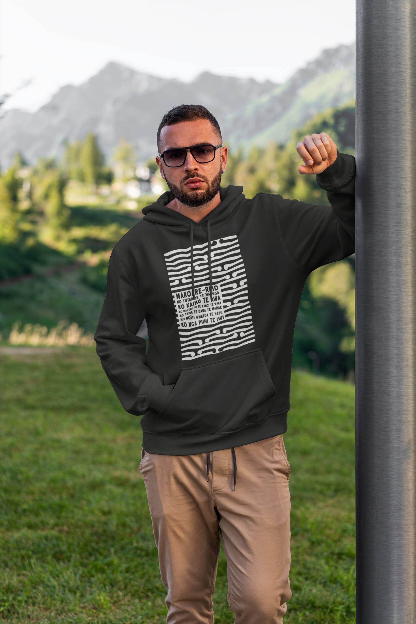 Tane man wearing a custom koru pepeha hoodie with grass in the background