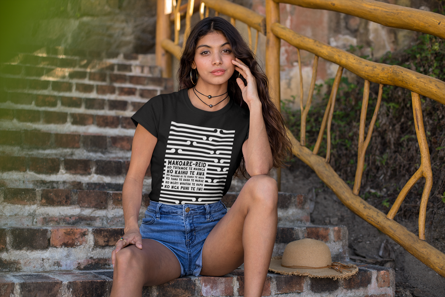 Beautiful maori woman sitting on steps wearing a custom pepeha tee by Mana Ake