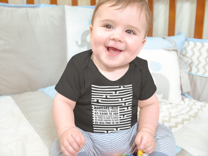 Cute baby sitting in his cot wearing a custom pepeha onsie and stripped pants