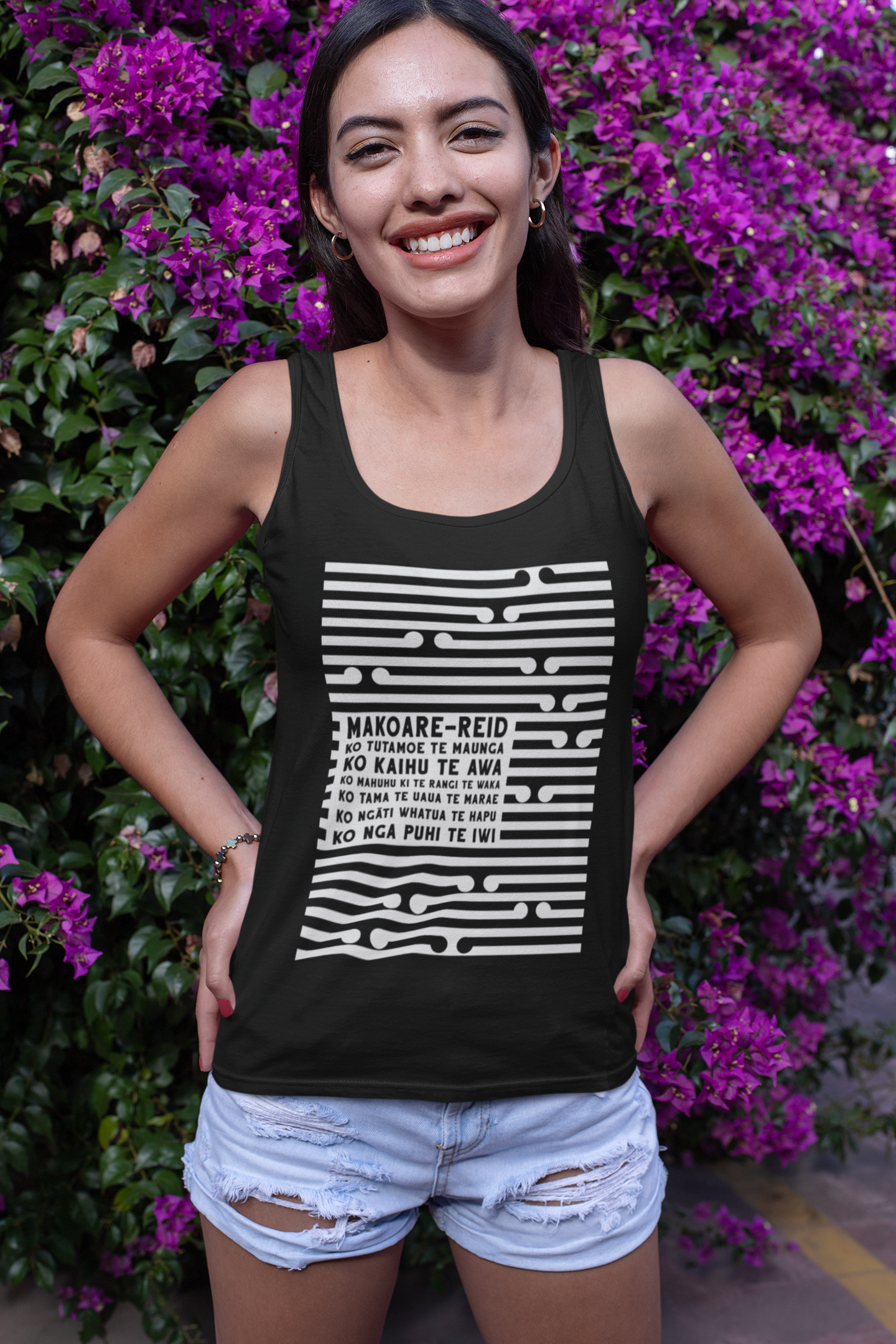 Beautiful maori women standing in front of a flowering plant, wearing a custom pepeha singlet by Mana Ake 